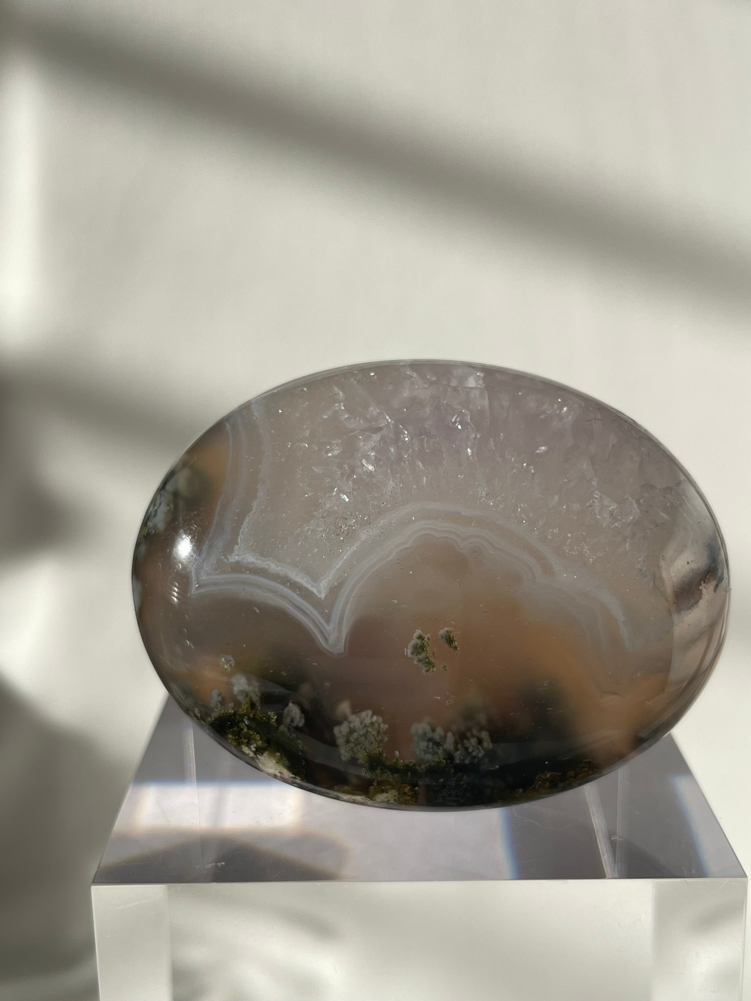 Scenic moss agate palm stone with soft hues and natural patterns, displayed on a clear pedestal.