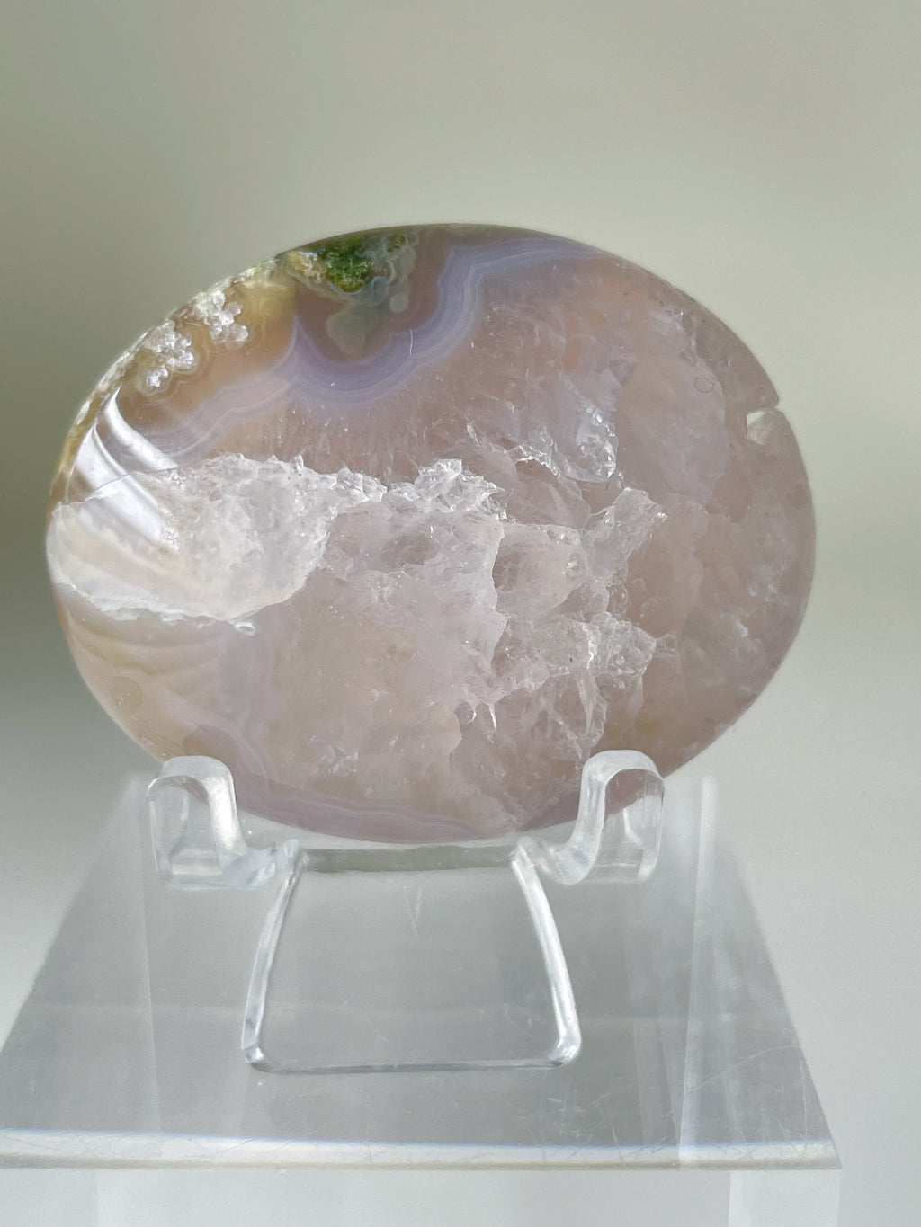Scenic moss agate palm stone displayed on a clear stand, showcasing its unique patterns and colors.