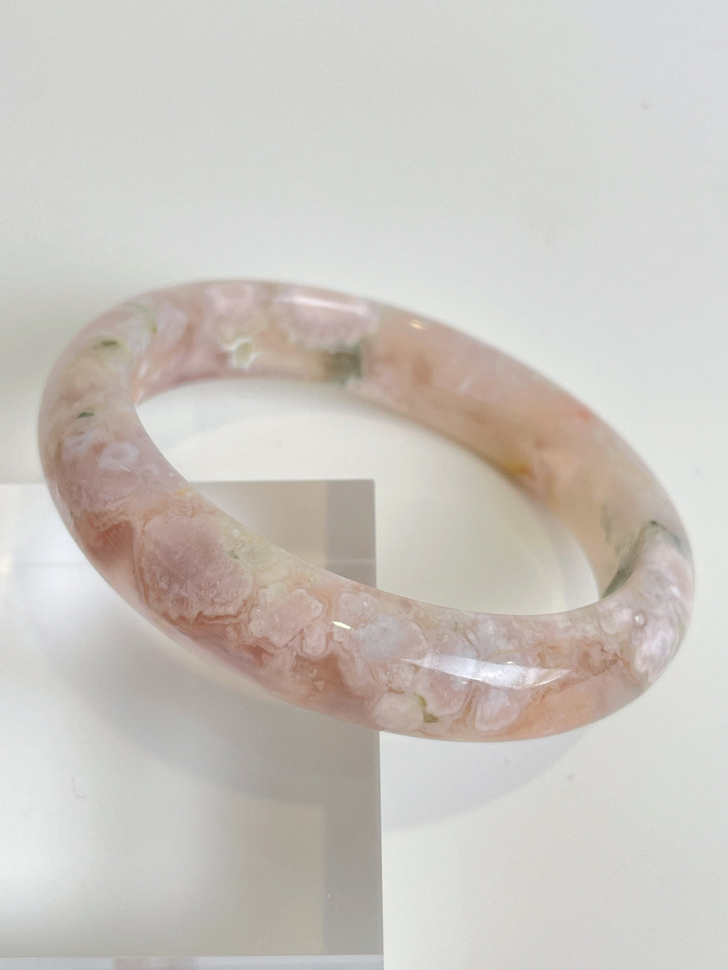 Beautiful flower agate bangle featuring soft pink hues and natural patterns, displayed on a clear stand.