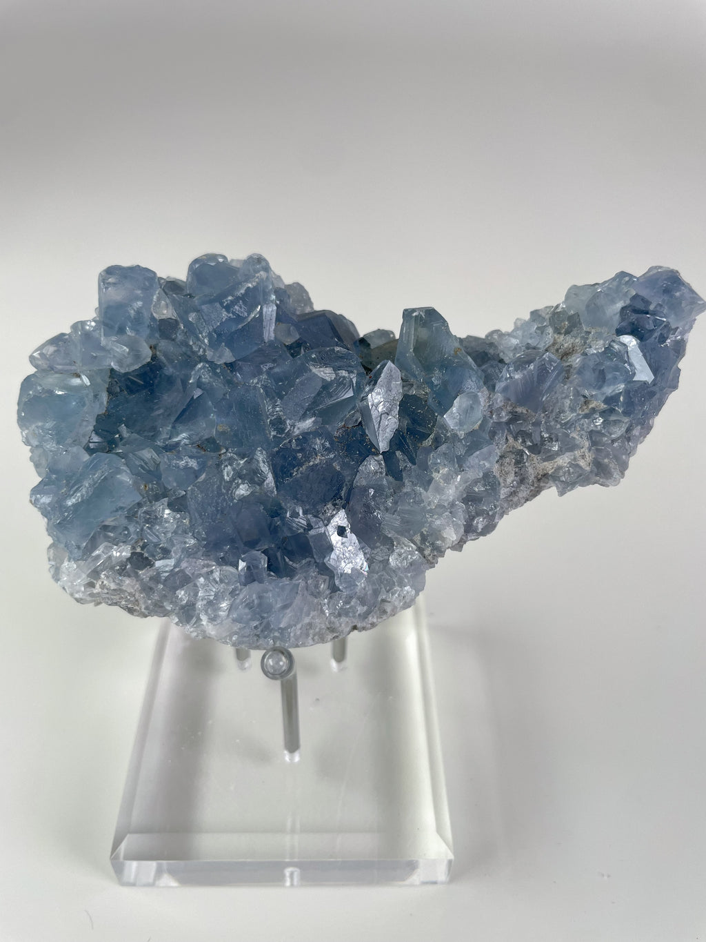 Beautiful Madagascar celestite cluster with shimmering blue crystals, displayed on a clear stand.