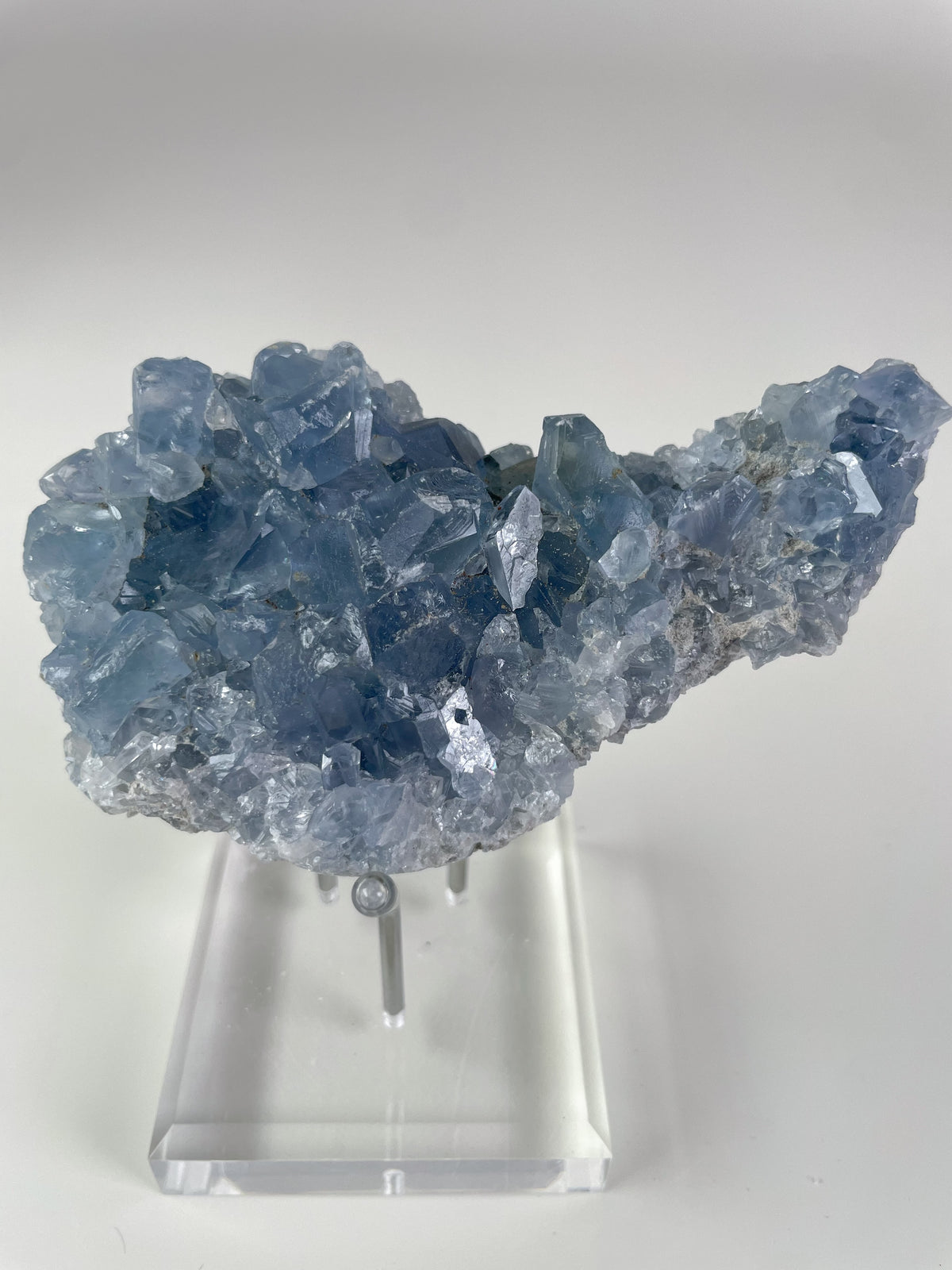 Beautiful Madagascar celestite cluster with shimmering blue crystals, displayed on a clear stand.