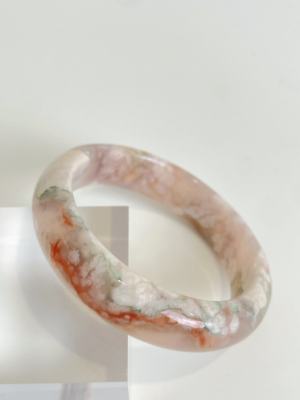 Beautiful flower agate bangle showcasing soft pink and white patterns, resting on a clear display.
