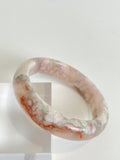 Beautiful flower agate bangle showcasing soft pink and white patterns, resting on a clear display.