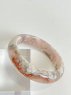 Beautiful flower agate bangle showcasing soft pink and white patterns, resting on a clear display.
