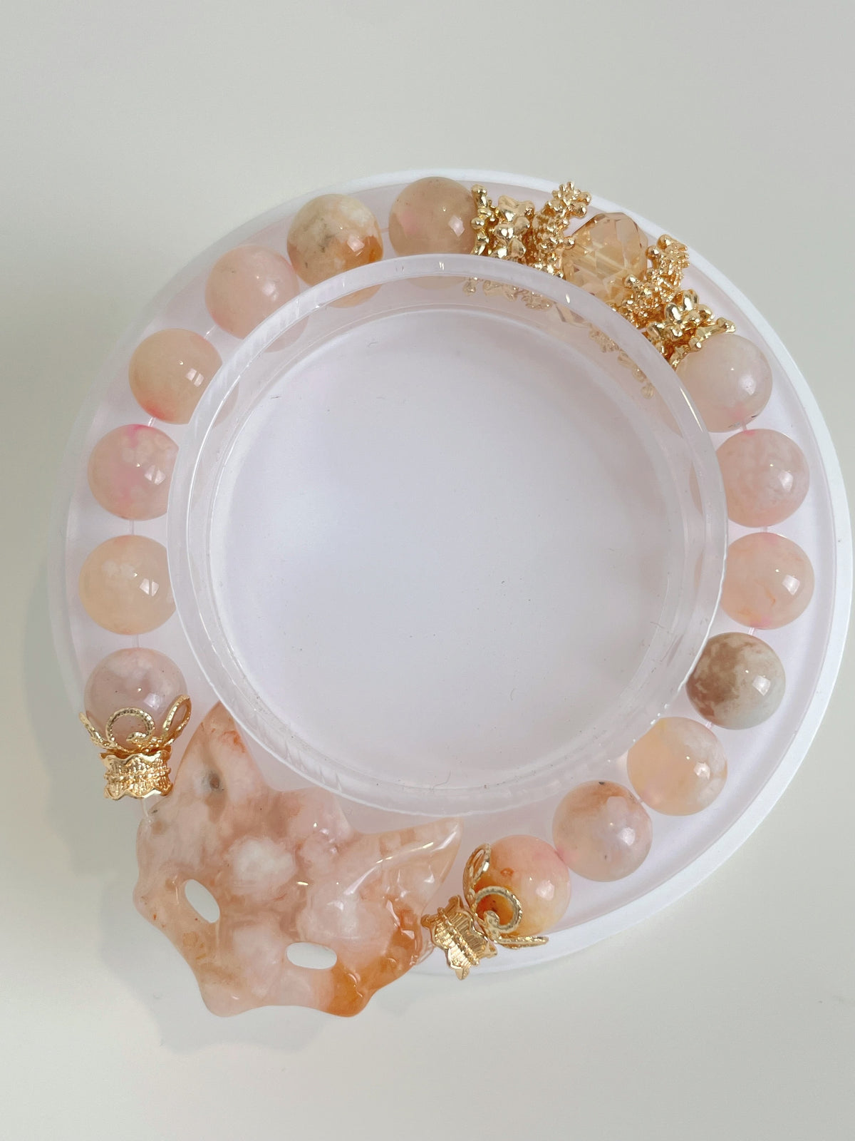 Flower agate bracelet featuring 9mm beads and a fox charm, accented with gold details, displayed on a round tray.