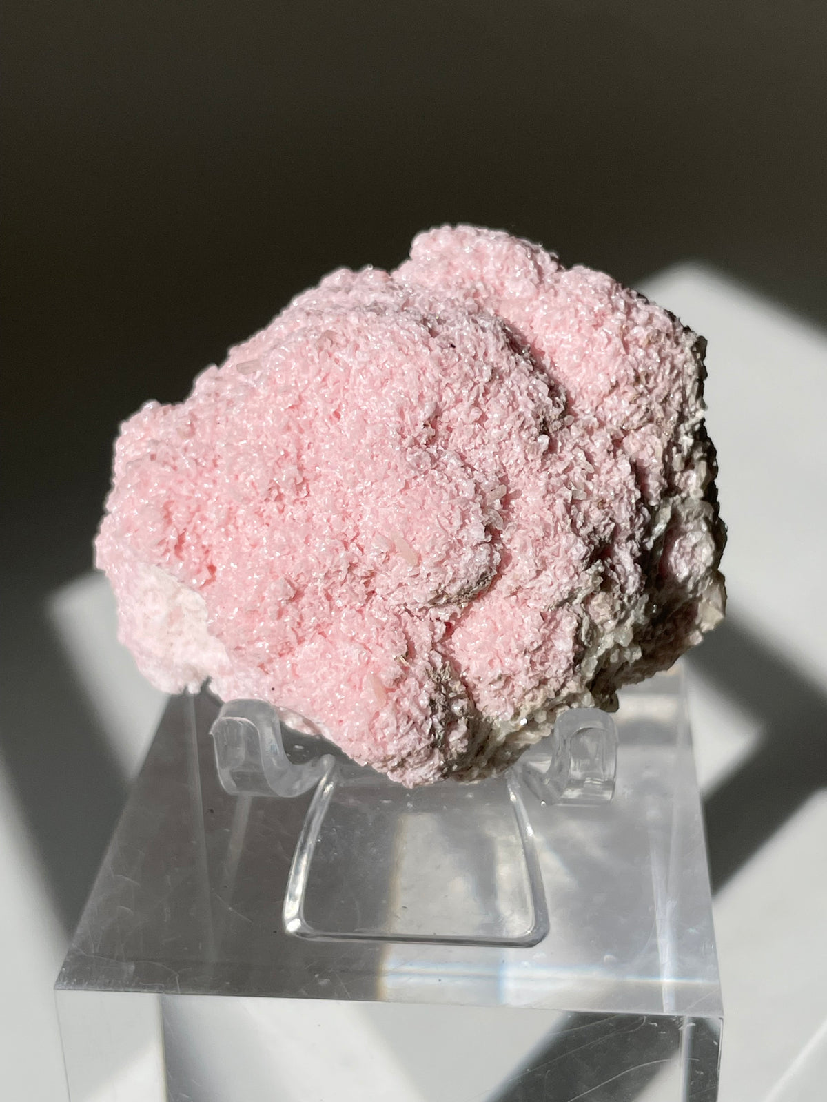 Beautiful rhodochrosite cluster with a soft pink hue, displayed on a clear stand, showcasing its unique texture.