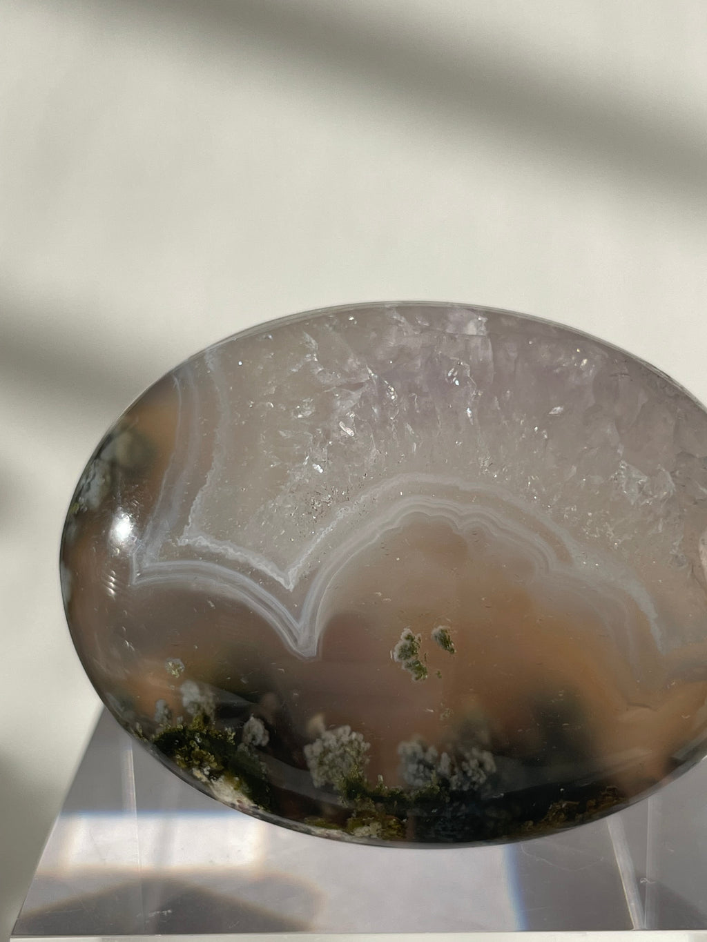 Scenic moss agate palm stone with earthy tones and unique patterns, displayed elegantly on a clear stand.