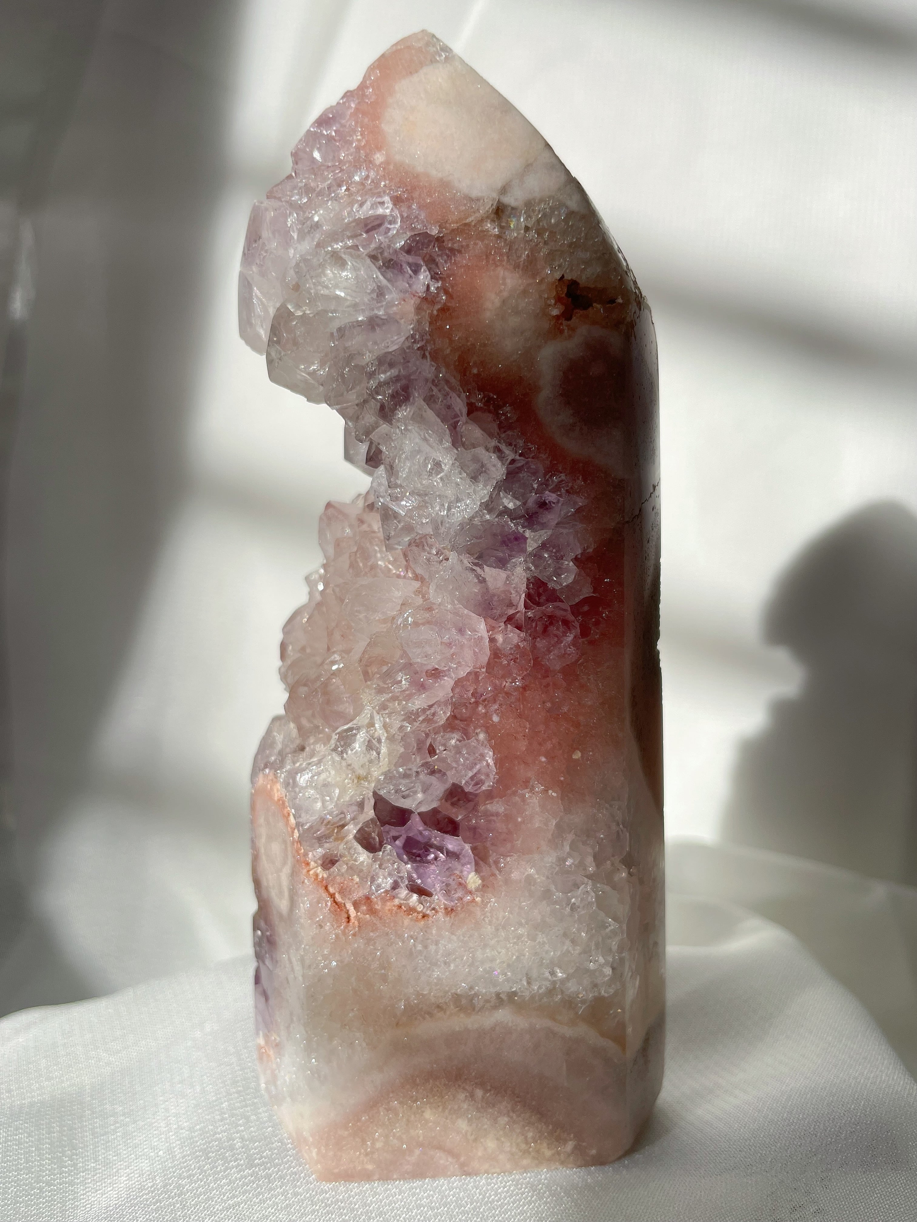 Beautiful purple and pink amethyst tower with sparkling crystal formations, softly illuminated by natural light.