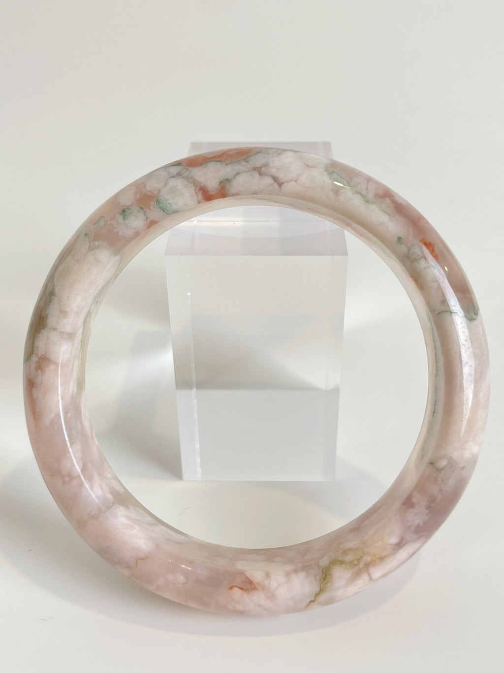 Beautiful flower agate bangle featuring soft pink and green hues, displayed on a clear stand.