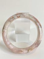Beautiful flower agate bangle featuring soft pink and green hues, displayed on a clear stand.