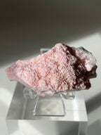 Rhodochrosite cluster with a soft pink hue, displayed on a clear stand, showcasing its textured surface.