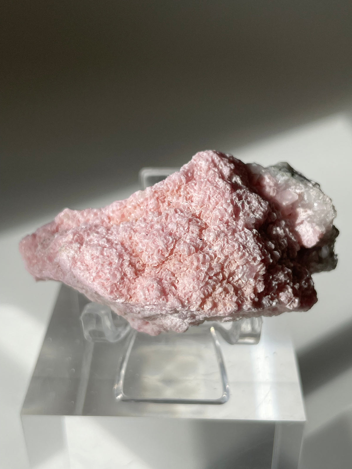Rhodochrosite cluster with a soft pink hue, displayed on a clear stand, showcasing its textured surface.