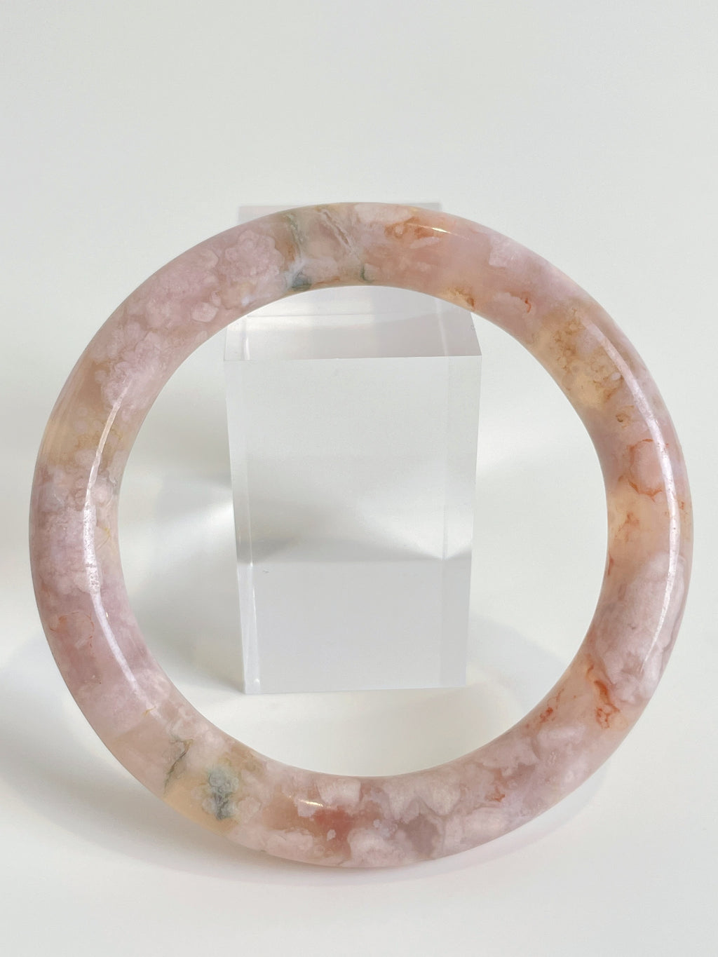 Beautiful flower agate bangle showcasing soft pink hues and natural patterns, displayed beside a clear stand.