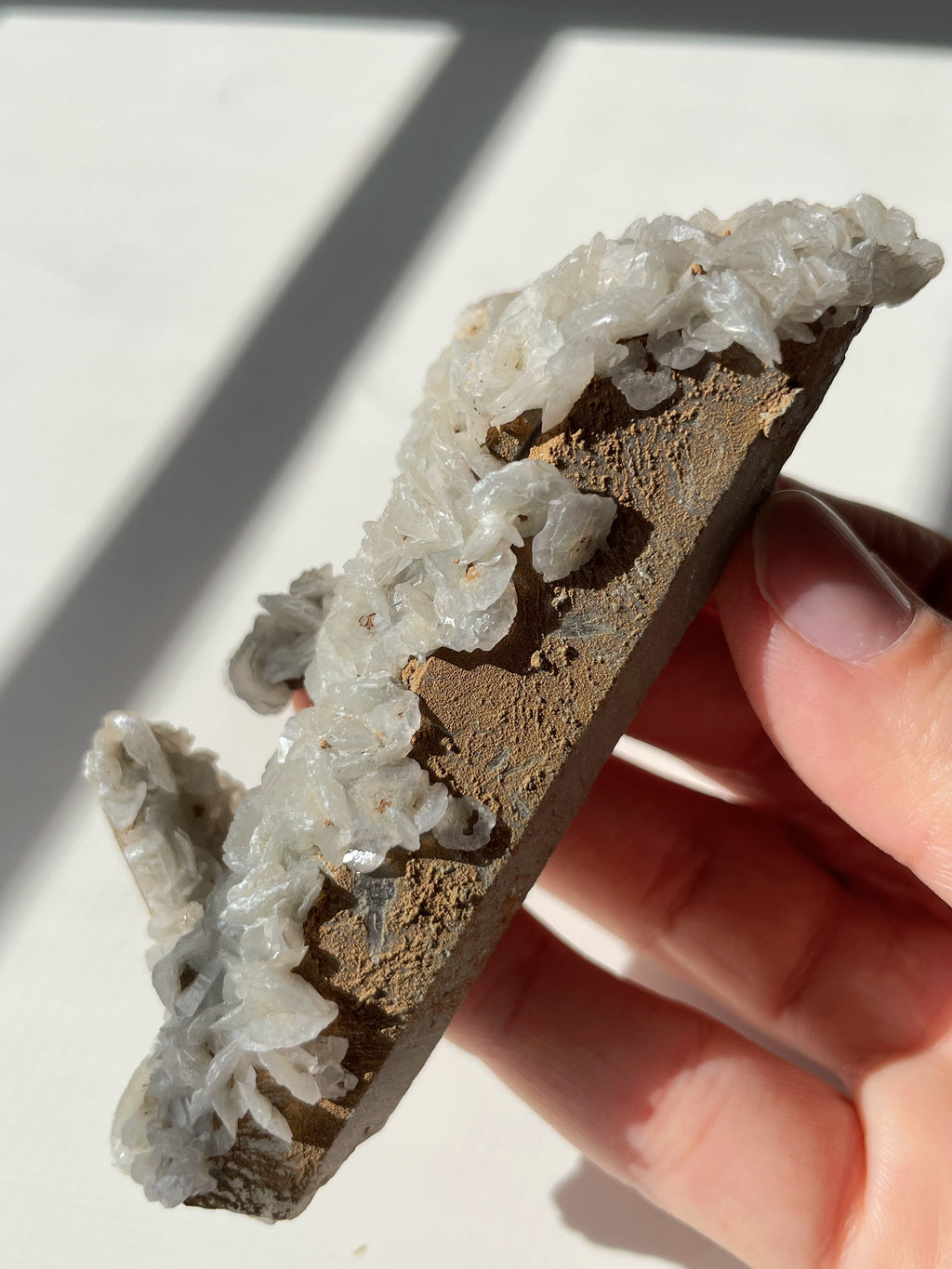 Beautiful crystal specimen featuring flower calcite on chlorite-included quartz, held in a hand with natural lighting.