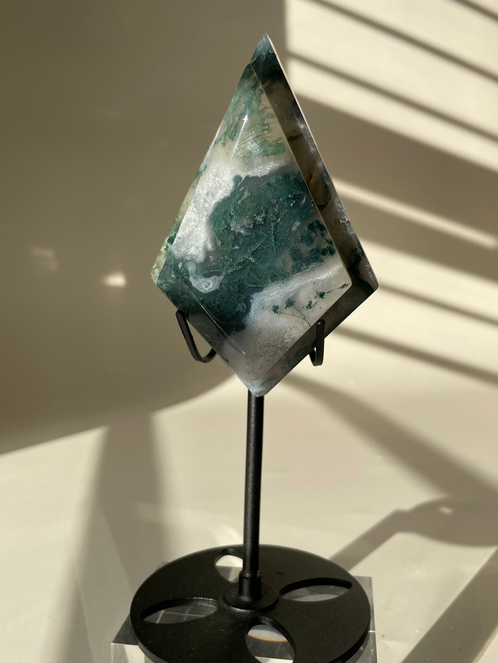 Scenic moss agate crystal specimen displayed on a sleek black stand, showcasing its unique green and white patterns.