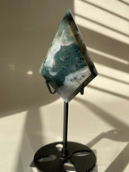 Scenic moss agate crystal specimen displayed on a sleek black stand, showcasing its unique green and white patterns.