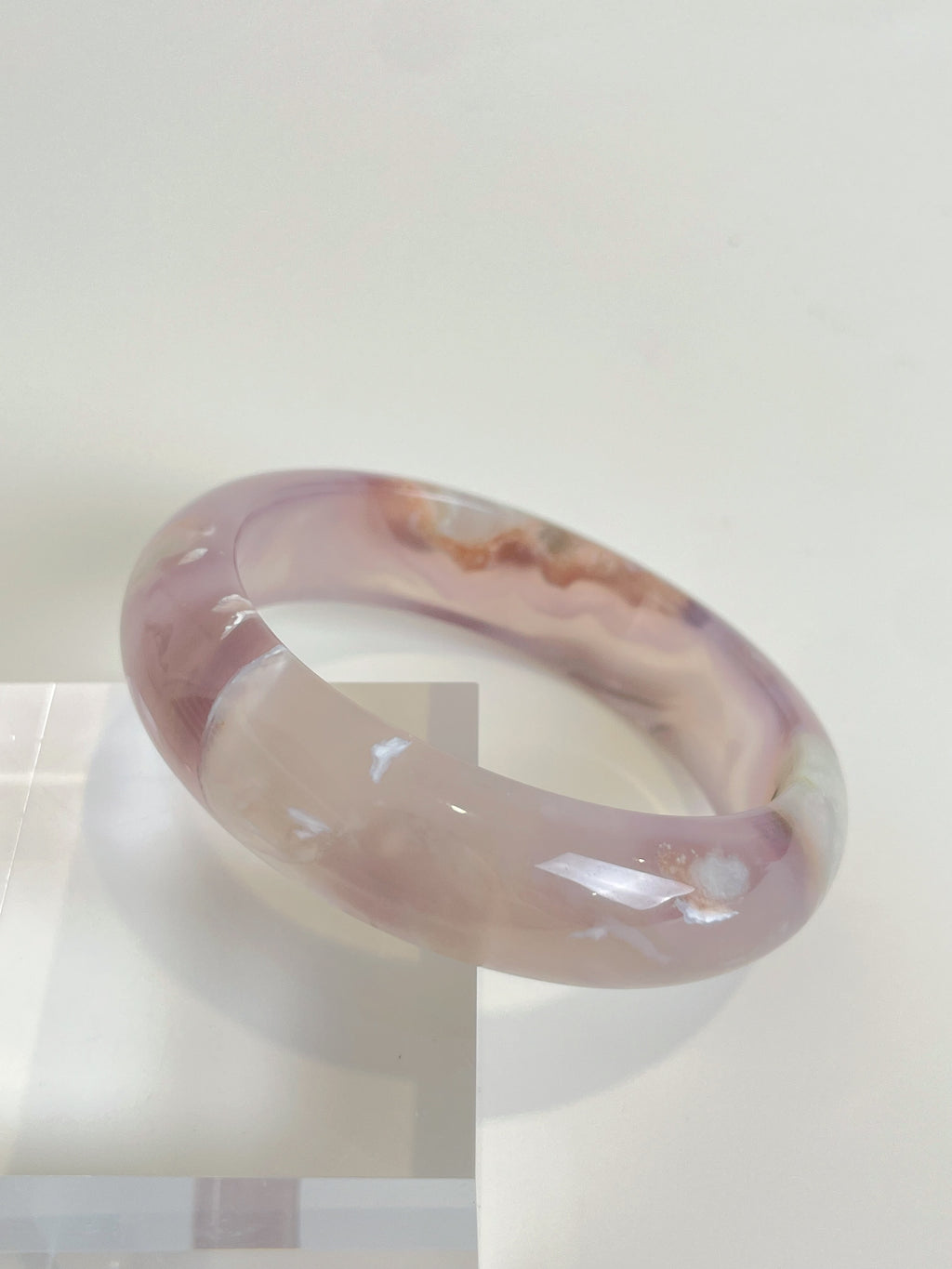 Beautiful flower agate bangle showcasing soft pink hues and unique patterns, resting on a clear display.