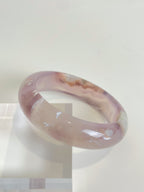 Beautiful flower agate bangle showcasing soft pink hues and unique patterns, resting on a clear display.