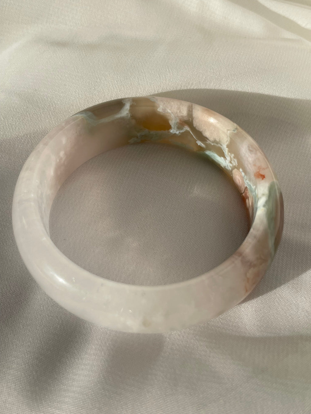 Beautiful flower agate bangle showcasing soft pink and earthy tones, resting on a light fabric background.