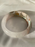 Beautiful flower agate bangle showcasing soft pink and earthy tones, resting on a light fabric background.