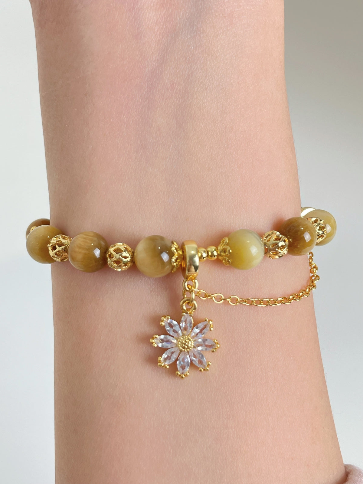 Gold Tiger's Eye bracelet featuring 8.3mm beads and a delicate flower charm, elegantly worn on a wrist.