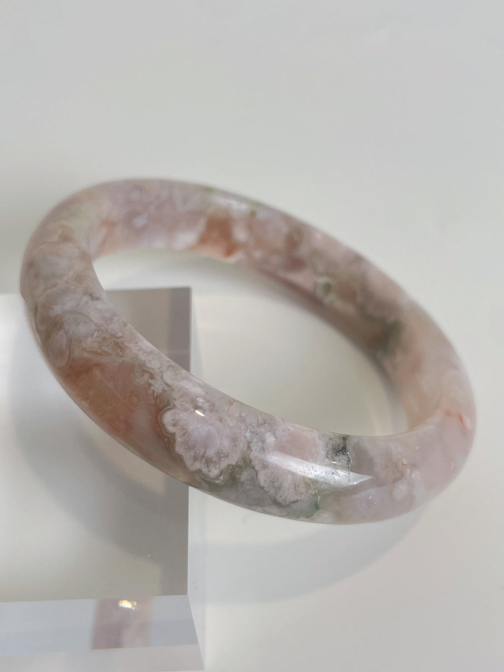 Beautiful flower agate bangle with soft pink and green hues, resting on a clear display stand.