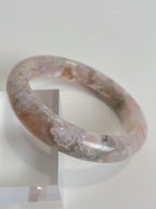 Beautiful flower agate bangle with soft pink and green hues, resting on a clear display stand.