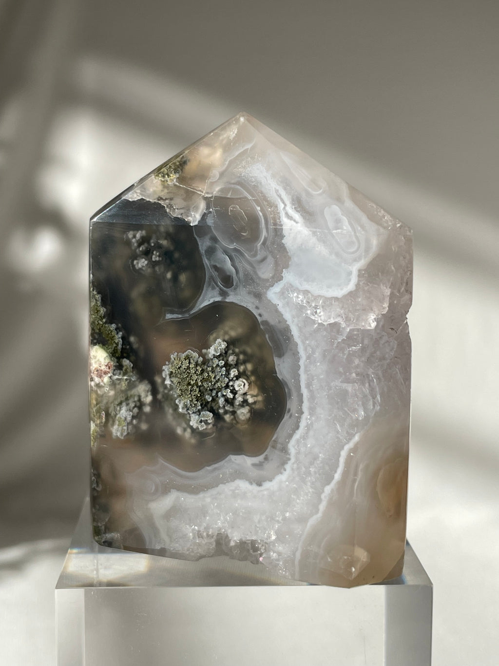 Scenic moss agate tower showcasing intricate patterns and earthy tones, resting on a clear base.