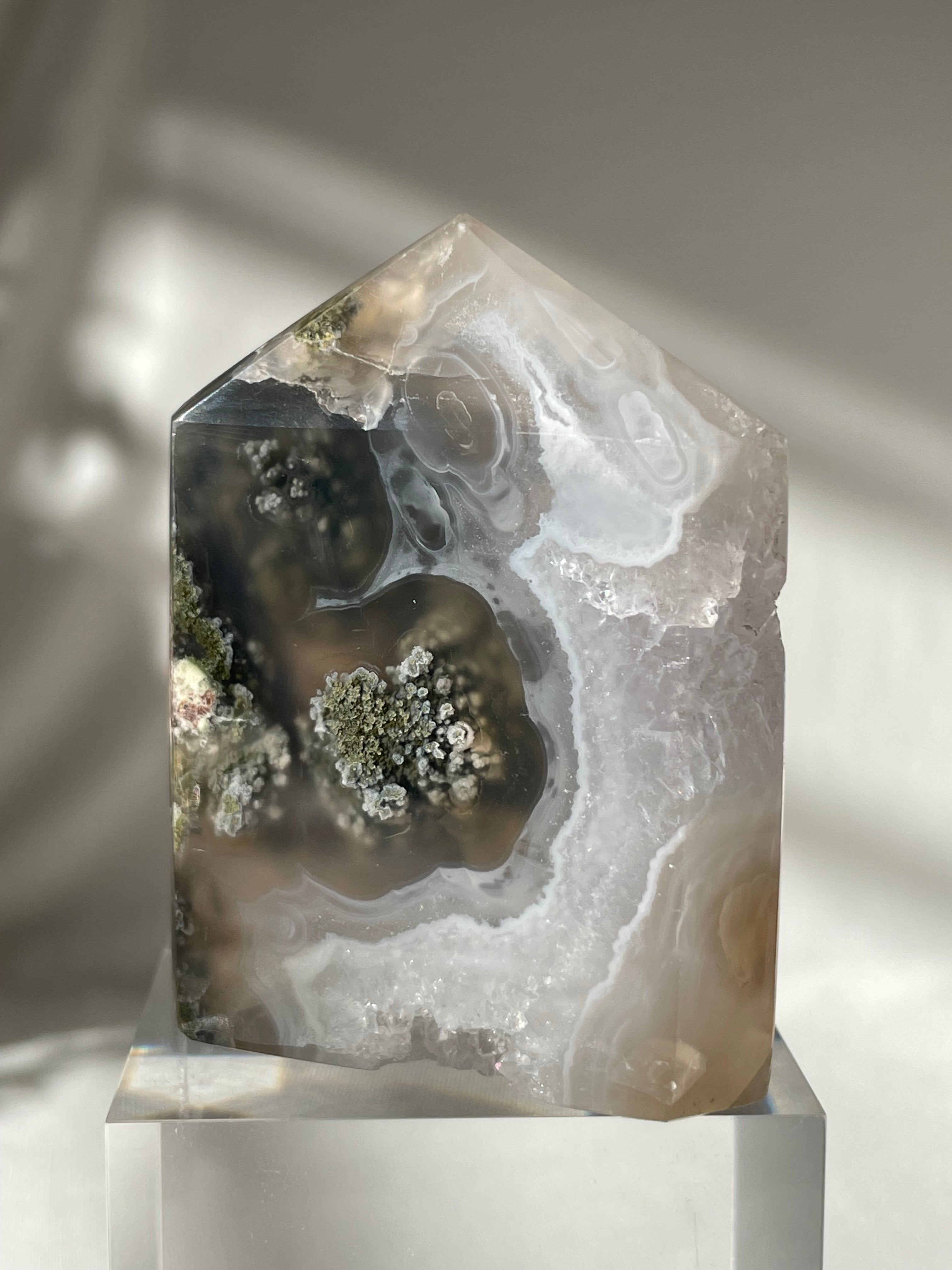 Scenic moss agate tower showcasing intricate patterns and earthy tones, resting on a clear base.