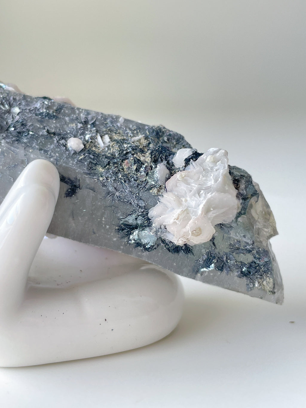 Beautiful pink petal calcite on quartz, showcasing intricate textures and colors, displayed on a white hand sculpture.