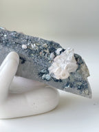 Beautiful pink petal calcite on quartz, showcasing intricate textures and colors, displayed on a white hand sculpture.