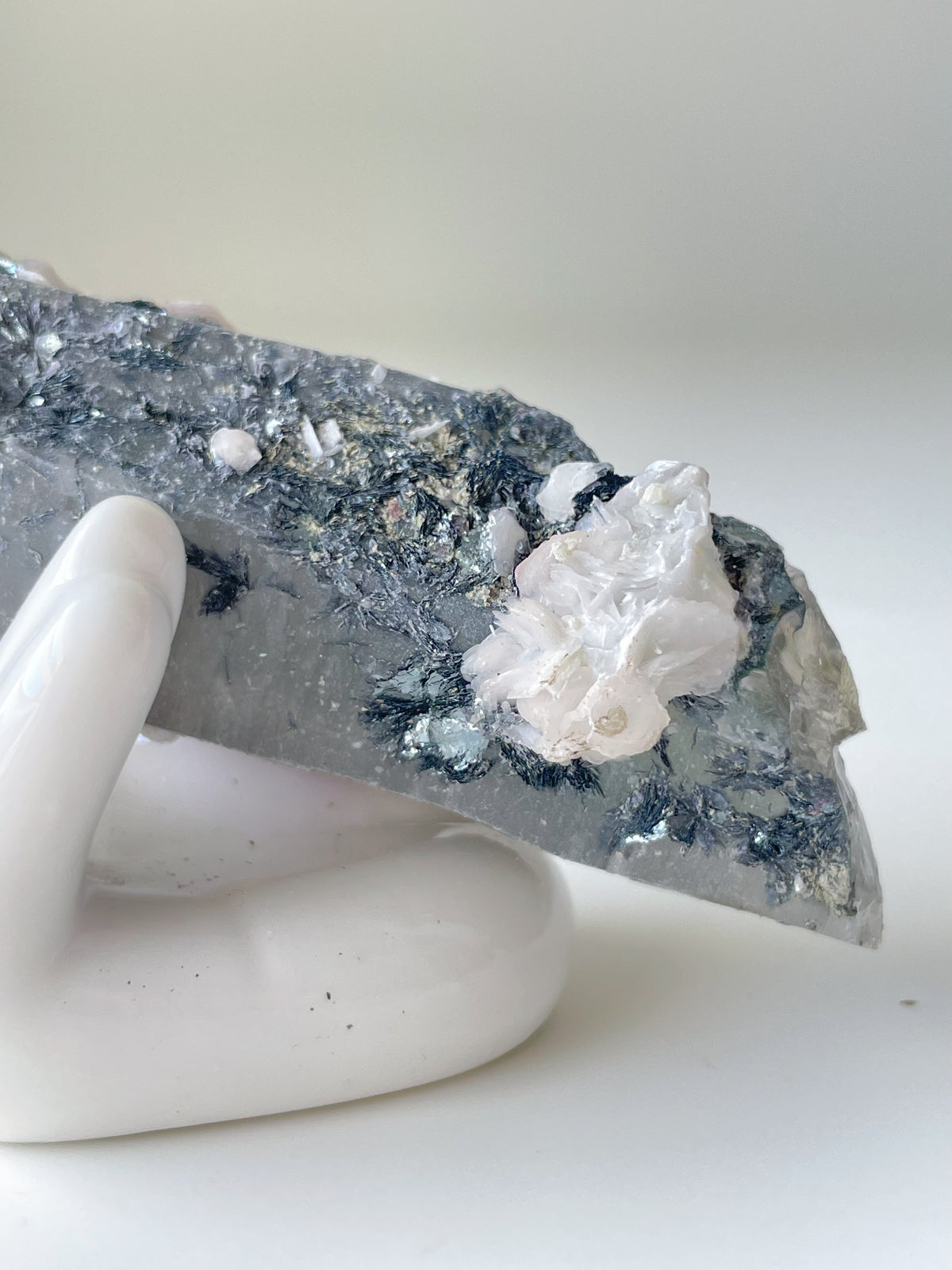 Beautiful pink petal calcite on quartz, showcasing intricate textures and colors, displayed on a white hand sculpture.