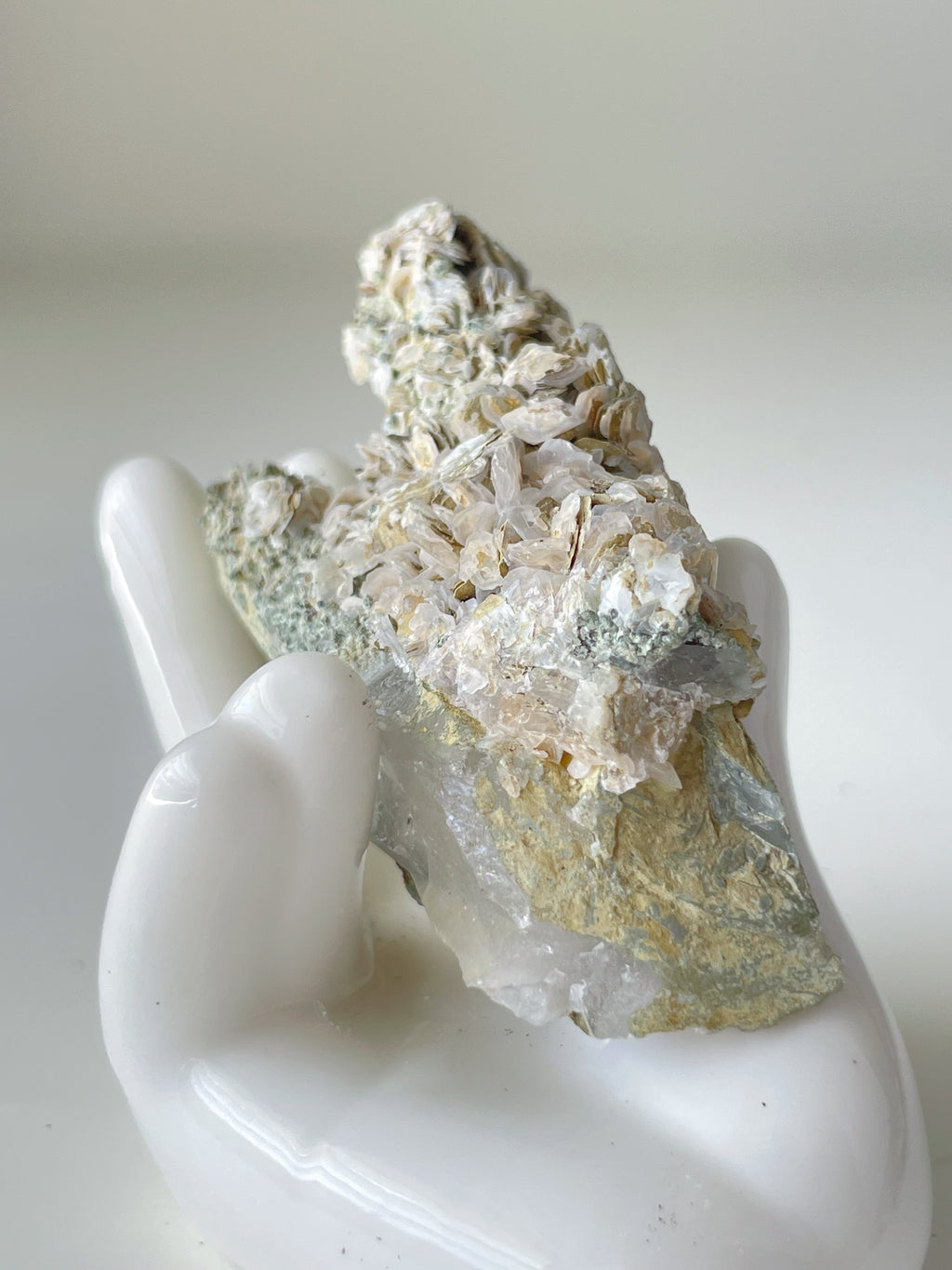 Rosette petal calcite specimen resting in a white ceramic hand, showcasing its unique textures and colors.