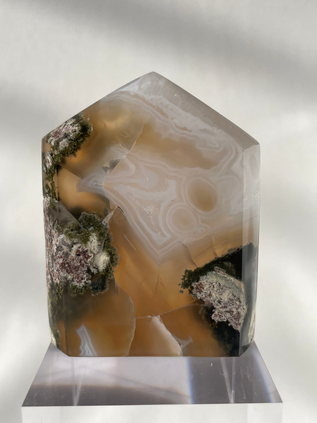 Scenic moss agate tower with earthy tones and unique patterns, displayed on a clear base.