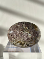 Scenic moss agate palm stone with intricate patterns, resting on a clear display stand, showcasing its natural beauty.