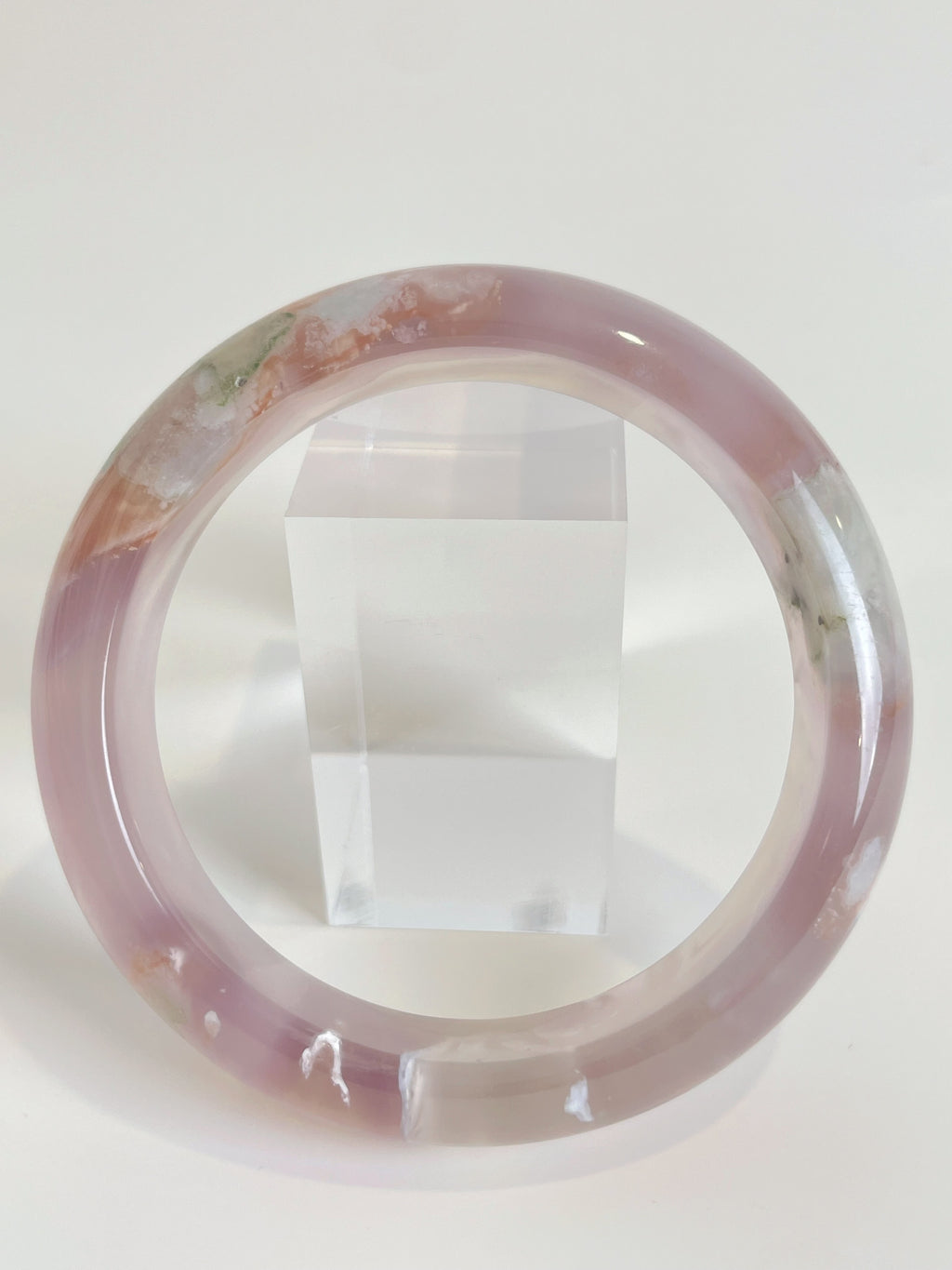Flower agate bangle featuring soft pink hues and natural patterns, displayed beside a clear acrylic stand.