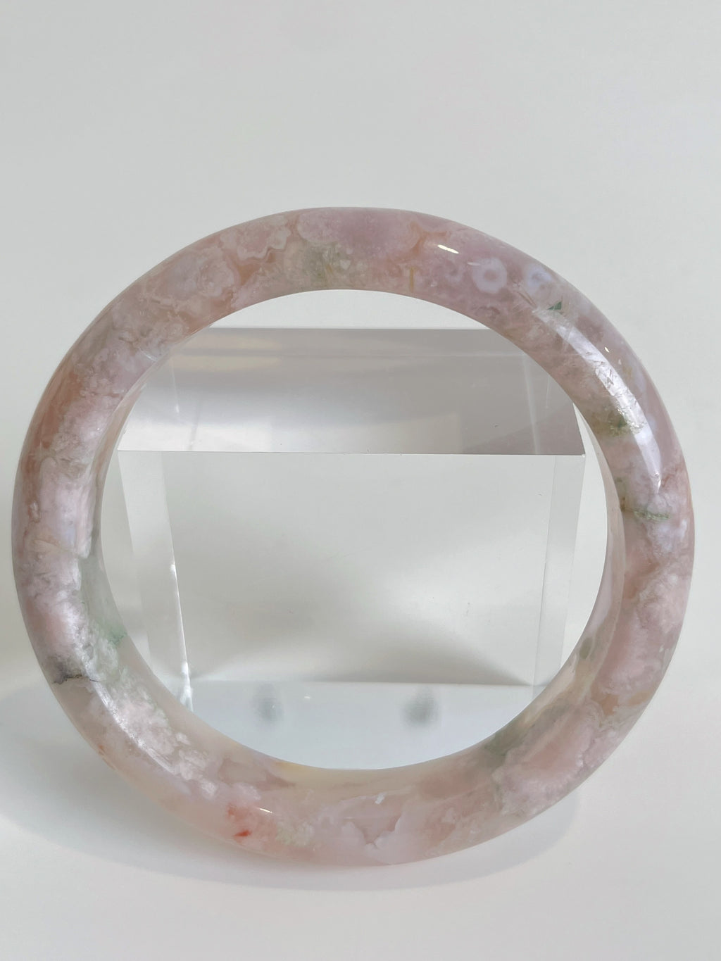 Beautiful flower agate bangle showcasing soft pink hues and subtle green patterns, displayed on a clear stand.