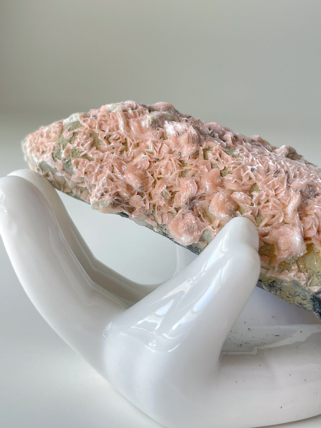 Beautiful pink petal calcite specimen resting on a white hand sculpture, showcasing intricate textures.