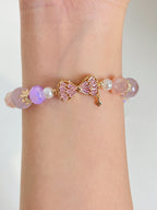 A delicate bracelet featuring pink and purple beads, adorned with a gold bow charm and pearl accents.