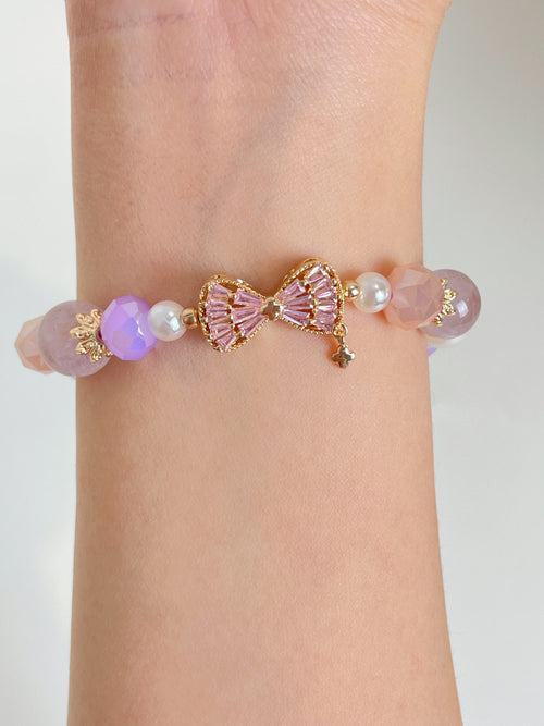 A delicate bracelet featuring pink and purple beads, adorned with a gold bow charm and pearl accents.