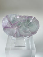 Beautiful fluorite crystal specimen with shades of purple and green, displayed on a clear stand.