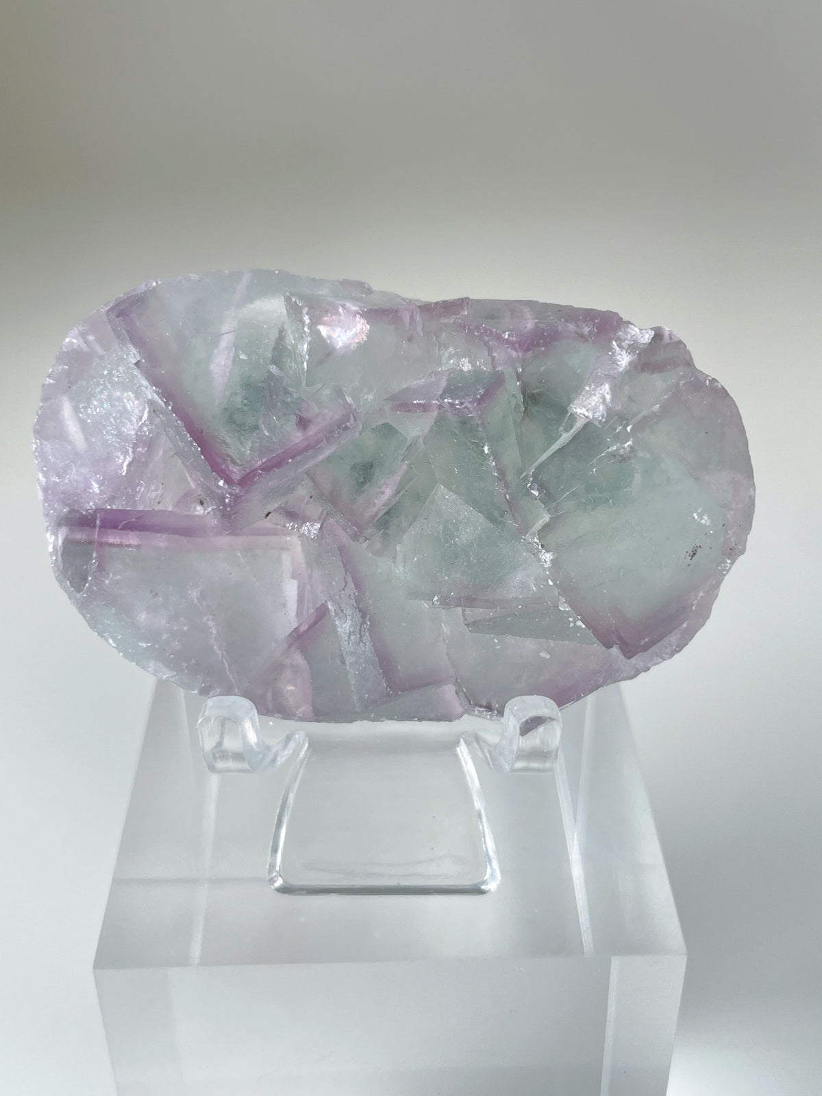 Beautiful fluorite crystal specimen with shades of purple and green, displayed on a clear stand.