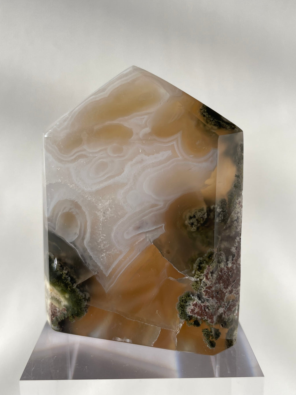 Scenic moss agate tower with earthy tones and intricate patterns, displayed on a clear stand.