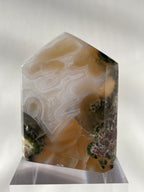Scenic moss agate tower with earthy tones and intricate patterns, displayed on a clear stand.