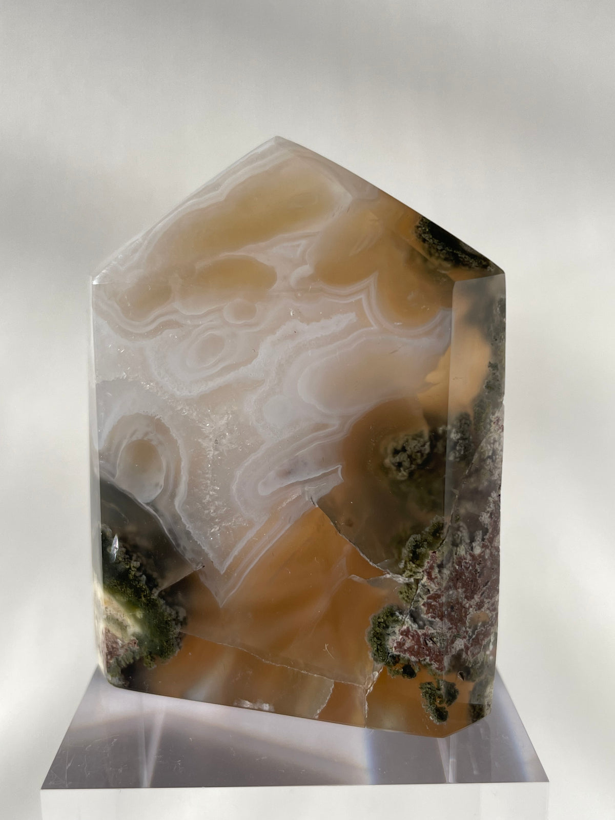 Scenic moss agate tower with earthy tones and intricate patterns, displayed on a clear stand.