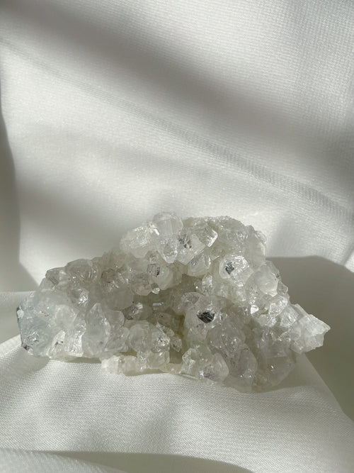 A sparkling apophyllite cluster with clear, crystalline formations resting on a soft white fabric.