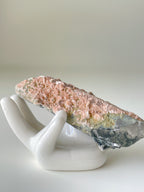 Beautiful pink petal calcite specimen resting on a white ceramic hand display, showcasing intricate textures.