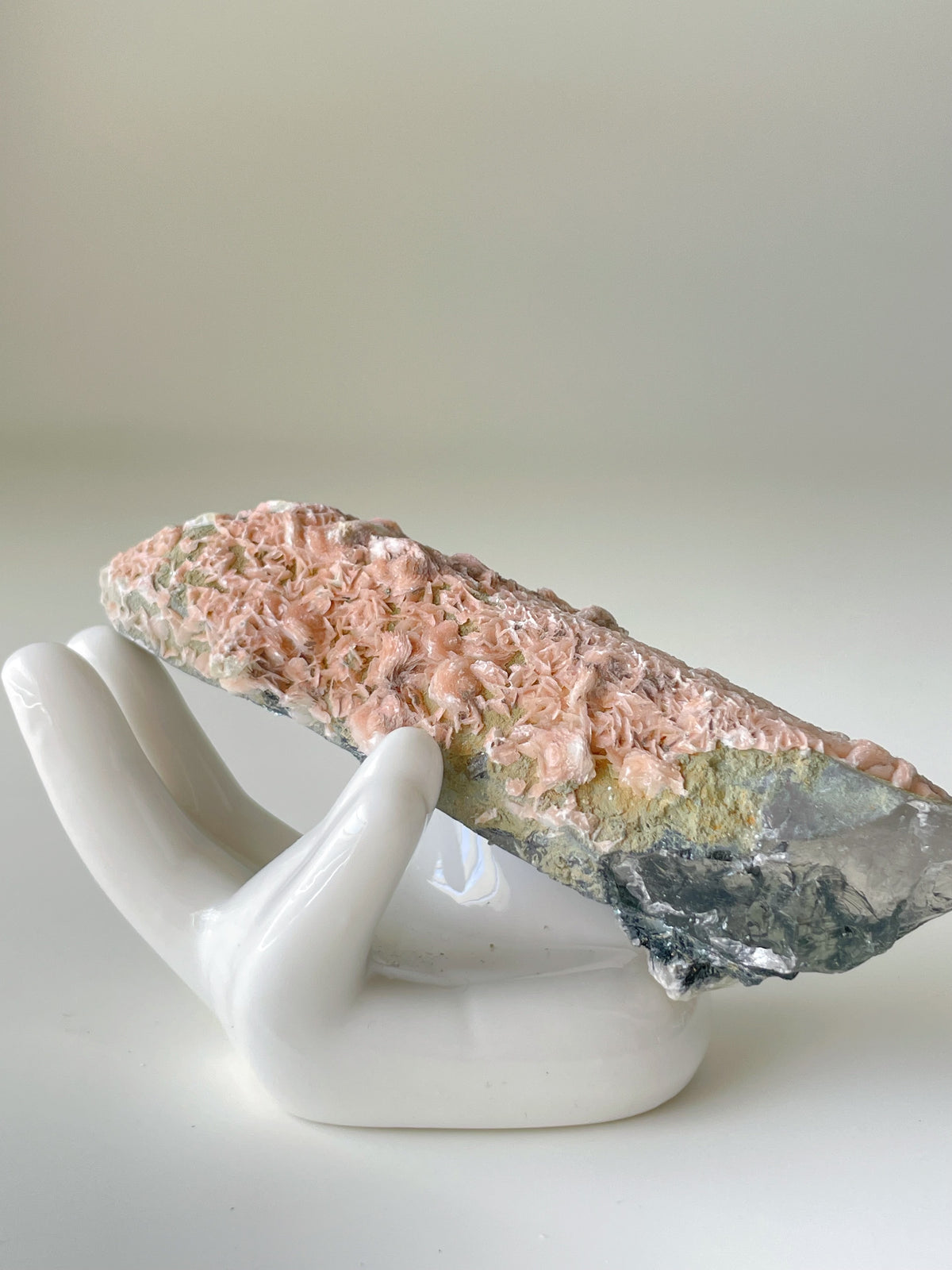 Beautiful pink petal calcite specimen resting on a white ceramic hand display, showcasing intricate textures.