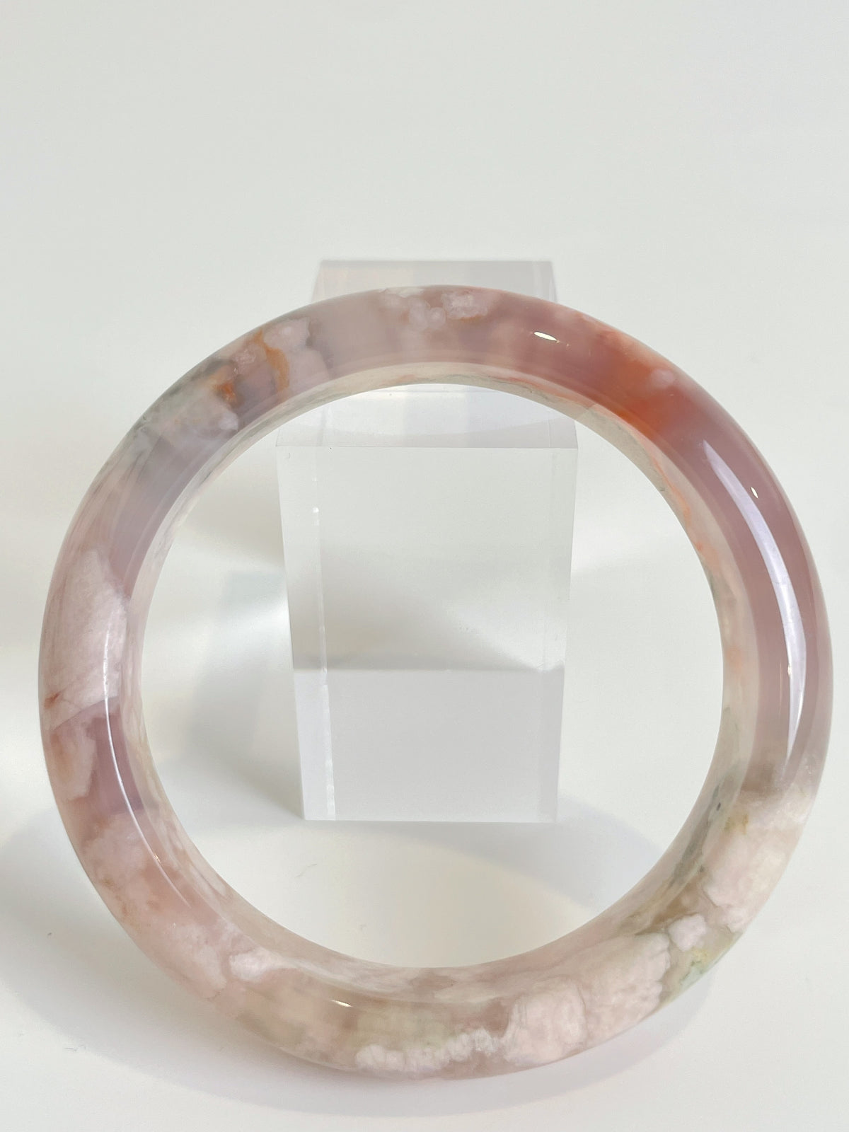 Beautiful flower agate bangle showcasing soft pink and white patterns, displayed on a clear stand.