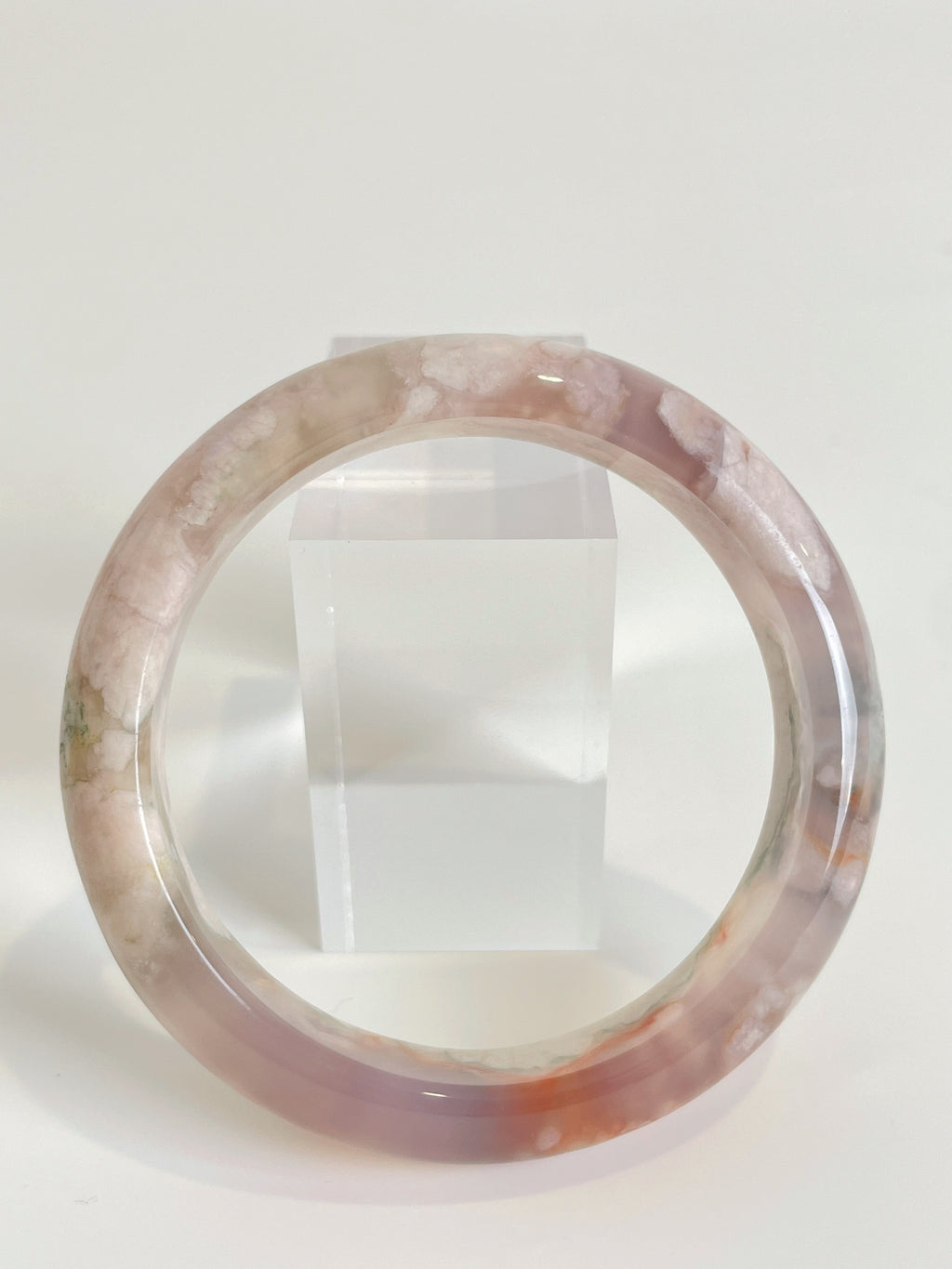 Beautiful flower agate bangle with soft pink and cream hues, displayed on a clear stand.